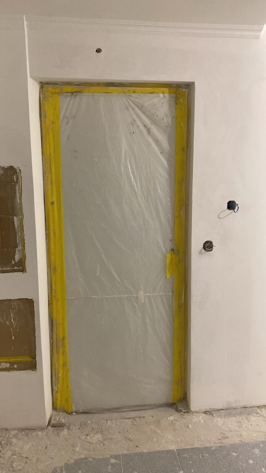 Porta protegida com plástico durante a obra, com caixas elétricas e cabos preparados na parede ao lado