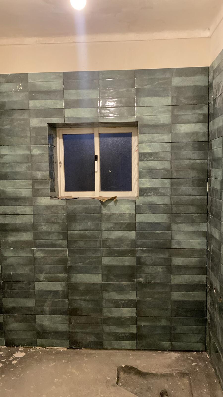 Casa de banho em remodelação com azulejo verde nas paredes e caixas preparadas antes dos acabamentos
