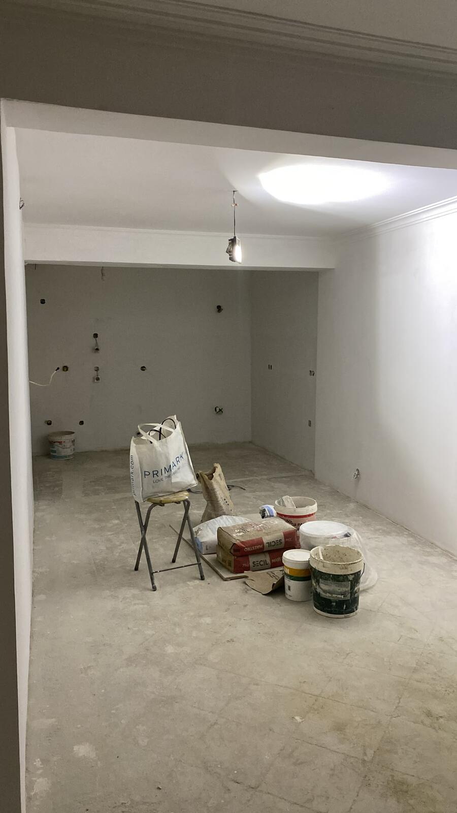 Sala estucada em obra com caixas elétricas embutidas nas paredes e materiais de construção no chão